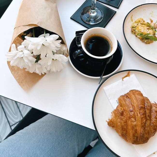 Top view of coffee, croissant, and flowers on a cafe table, creating a warm, inviting breakfast scene.